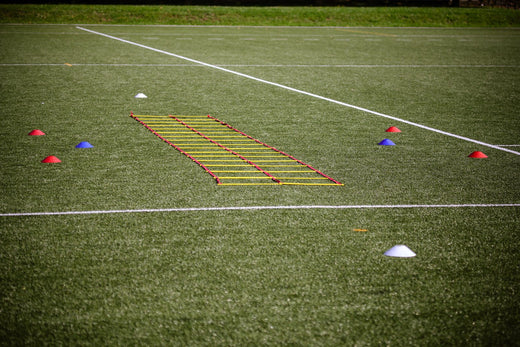 Yellow and red agility ladder with red, blue and white marker cones set out on an artificial football pitch